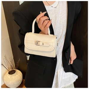 Detail of cream patent leather handbag featuring metal buckle strap and top handle
