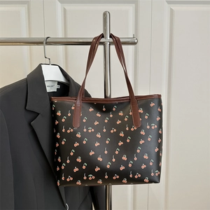 Minimalist black tote bag featuring a vibrant red cherry print and brown leather handles