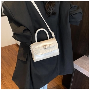 Close-up of creamy white patent leather handbag with metallic buckle and slim strap
