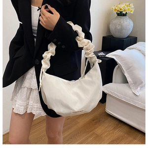 Sac bandoulière demi-lune crème avec bandoulière plissée dans un décor intérieur