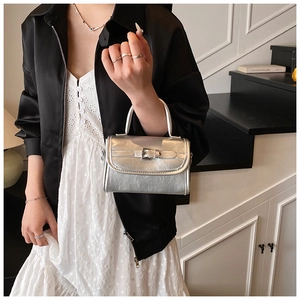 Detail of a shiny silver patent leather mini handbag with a decorative buckle held by a model