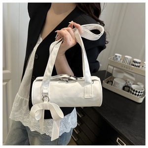 Detail view of a white Boston barrel bag with a bow charm held by a model in a modern room