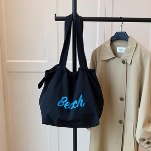 Black canvas tote bag with blue Beach text and drawstring closure on clothes rack