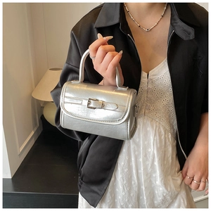 Detail of a silver patent leather handbag featuring a sleek metallic finish and top handle