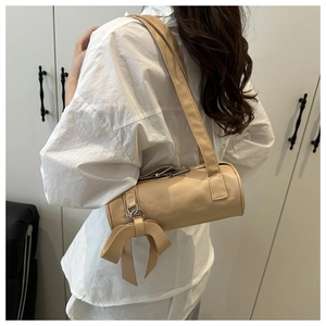 Side view of beige Boston barrel bag with bow charm detail and wide shoulder strap