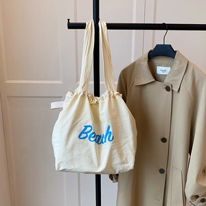 Close-up of off-white canvas tote bag with blue Beach lettering hanging on a rack