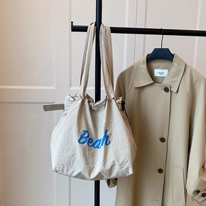 Detail of beige canvas tote bag with blue Beach lettering and wide shoulder strap