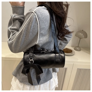 Détail d'un sac cylindrique noir avec un grand nœud et texture en cuir mat de qualité