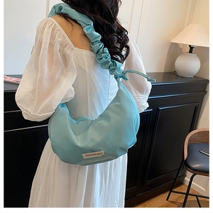 Détail du sac croissant plissé bleu clair avec bandoulière et étiquette de mode