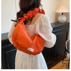 Sac hobo orange avec bandoulière plissée et étiquette de mode porté par un mannequin