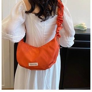 Détail du sac croissant orange avec bandoulière à volants et étiquette mode