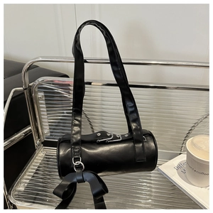 Détail d'un sac bandoulière cylindrique noir avec un grand nœud et des boucles argentées