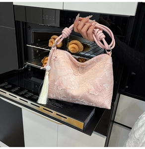 Detail of light pink tote bag featuring butterfly embroidery and fringe pendant