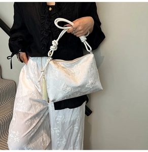 Detail of white lace tote bag featuring 3D butterfly embroidery and green tassel charm