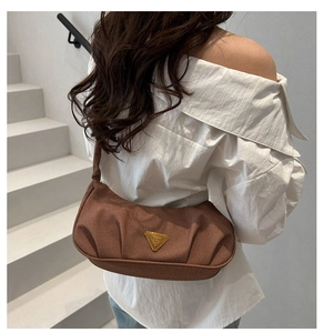 Close-up of pleated brown crescent bag featuring a metallic triangular logo plaque detail