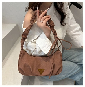 Detailed view of brown canvas hobo bag with ruffled handle and golden triangular emblem