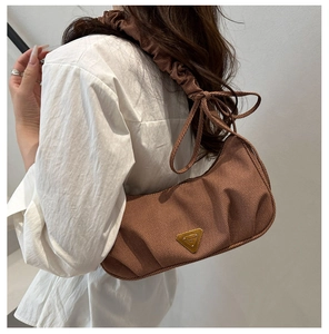 Detail view of coffee brown canvas bag showing pleated texture and gold triangular logo