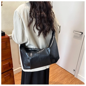 Rear view of a model wearing a large black soft leather dumpling bag with pleated texture