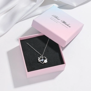 Macro shot of silver heart necklace with white shell petals in a blue gradient gift box