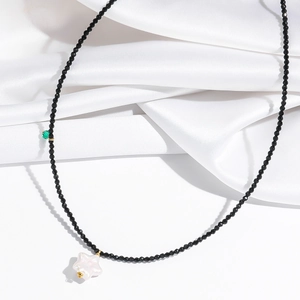 Detail of black multifaceted beads with white star pearl pendant on white silk fabric