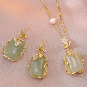Elegant gold jewelry set with green stones, leaf motif and pearls on silk