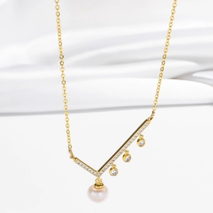 Détail du collier asymétrique en or avec pendentif en V, cristaux et perle d'eau douce