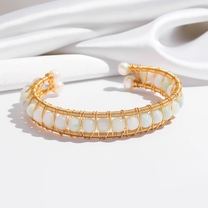 Close-up of gold wire-wrapped open bracelet with white pearls on elegant silk fabric