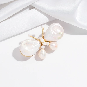 Macro detail of a butterfly brooch featuring baroque pearls and gold wire on white silk