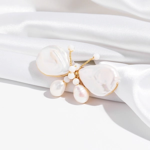 Macro detail of butterfly brooch with baroque pearls on white satin background