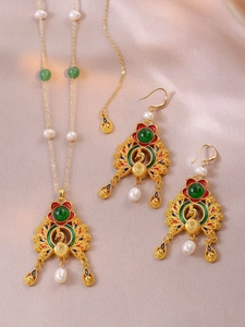 Detail of peacock enamel necklace and pearl earrings set on silk background