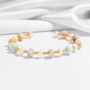 Detail of gold wire-wrapped bangle with pearls and colorful marbled stones on white silk