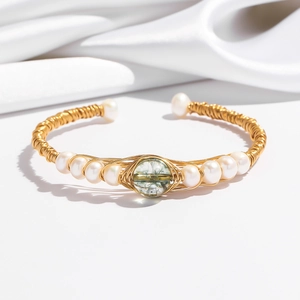 Detail of gold wire-wrapped bracelet with green crystal and white pearls on white silk