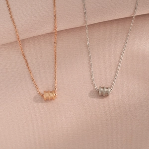 Minimalist cylinder pendant necklaces in rose gold and silver finishes on woven fabric