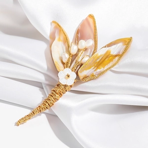 Macro shot of shell flower brooch with wire-wrapped gold base and pearls on silk