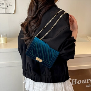 Dunkelblaue Samt-Umhängetasche mit goldener Kette am Modell für einen eleganten Look