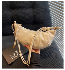 Detail of a creamy crescent croissant bag with vertical pleats and drawstring strap