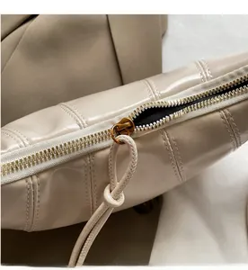 Detail of smooth gold zipper and beige glossy faux leather texture on the crossbody bag