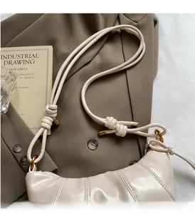Detail of a beige faux leather dumpling bag with quilted lines and knotted shoulder strap
