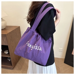 Detail of purple nylon tote bag with drawstring closure and white script lettering logo