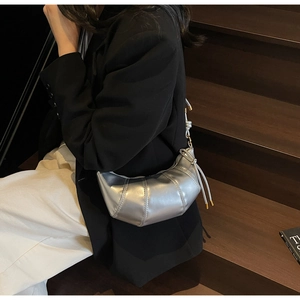 Silver crescent shoulder bag with metallic finish and drawstring detail shown on a model