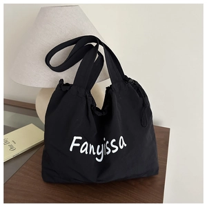Detail shot of a black canvas tote bag with drawstring closure on a wooden desk