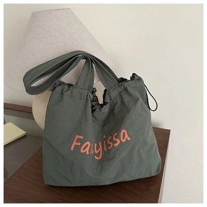 Detail of a large dark green nylon tote bag with orange text on a wooden table