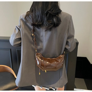 Detail view of a dark brown croissant crossbody bag worn on a grey blazer back