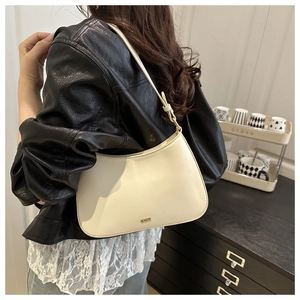 Détail d'un sac demi-lune crème avec logo MONER doré porté à l'épaule sur un blouson en cuir
