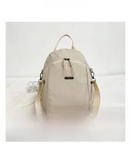 Detail of beige versatile backpack showing dual zippers and metal logo on a clean setup