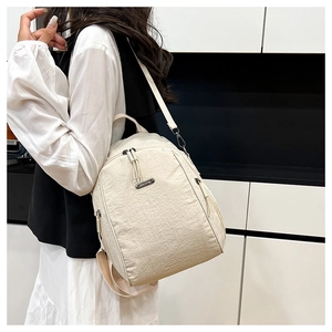 Detail of off-white nylon backpack showing wrinkled texture, top handle, and silver zippers