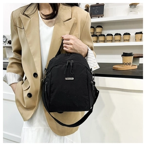 Detail of black nylon backpack featuring a metal logo plate and smooth zipper closure
