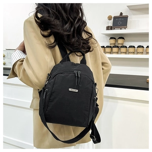 Detail of a versatile black nylon backpack with metal logo and adjustable straps on model