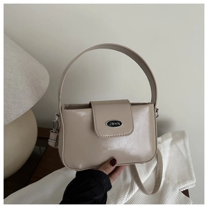 Détail du sac beige verni avec plaque logo métallique et finitions argentées chic