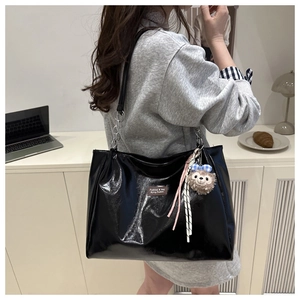 Detail of high-gloss black tote bag featuring a leather logo tag and plush hedgehog charm